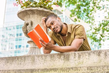 Giydiği yeşil kısa kollu gömlek, ayakta, ileri kampüste, duvar üzerine bükme geri New York'ta genç Afro-Amerikan üniversite öğrencisi eğitim eller kırmızı kitap, kafa çizilmemesi, okuma