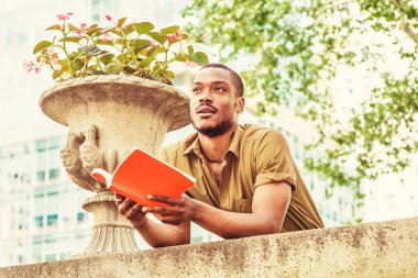 Giydiği yeşil kısa kollu gömlek, ayakta, ileri kampüste, duvar üzerine bükme geri New York'ta genç Afro-Amerikan üniversite öğrencisi eğitim kırmızı kitap, ararken, düşünme eller