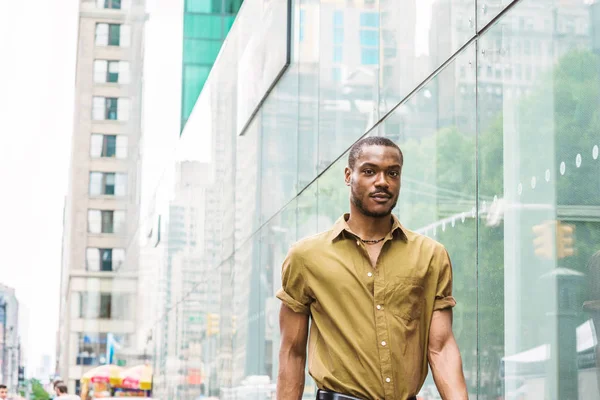 Genç Afro-Amerikan New York'ta seyahat pass cam duvar Midtown Manhattan'ın modern yüksek binalar ile sokakta yürürken yeşil kısa kollu gömlek giymiş yakışıklı.