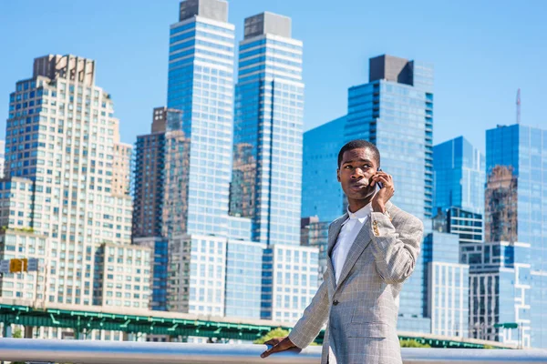 ニューヨークの旅行 若いアフリカ系アメリカ人のビジネスマンを着てブレザー 白いシャツ 携帯電話で話す 太陽の下でマンハッタンの高層ビルとビジネス街に立ってをパターン化 — ストック写真
