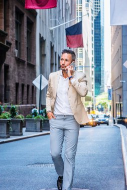 Sakal, küçük gri saçlı Genç Avrupa New York, cep telefonuyla konuşurken Manhattan, yüksek binalar ile dar sokakta yürürken bej ceket, gri pantolon, beyaz gömlek giymiş seyahat adam