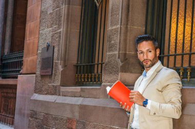 Genç Avrupa kırmızı kitap dışında Manhattan, New York, sakal, küçük gri saç ile okumak, windows, aydınlatma cam içinde duvar tarafından sokakta duran bej ceket, beyaz gömlek giymiş adam