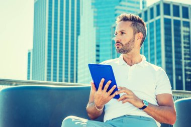 Modern okuma. Sakallı, küçük gri saç, Genç Avrupa beyaz Polo New York'ta yüksek binalar ile iş bölgesinde oturan gömlek, kol saati, tablet bilgisayar, okuma giymiş adam düşünme