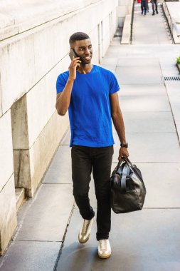 Okula dönüş. New York'ta eğitim, giyiyor mavi T takım, siyah pantolon, spor ayakkabı, çanta, cep telefonuyla konuşurken, ofis campu üzerinde binası dışında yürüyüş genç Afro-Amerikan üniversite öğrencisi