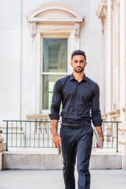 İş için gidin. Genç yakışıklı Doğu Hint Amerikan vintage ofis binası içinde yürüyüş sakallı adam New York'ta, giyen siyah gömlek, siyah pantolon, dizüstü bilgisayar, cep telefonu, holding eller çalışma.