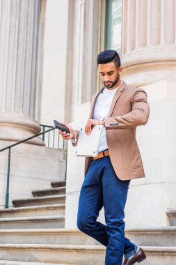 İşten sonra. Genç Doğu Hint Amerikalı kahverengi ceket, mavi pantolon giyiyor, dizüstü bilgisayar, telefon, kol, yetiştirme kol saati, seyir ofisinden merdivenlerden aşağı yürüyüş tutan işadamı sakallı,