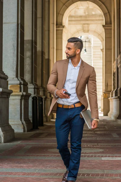 Adam sokak Fashion.Young Doğu Hint Amerikan seyahat, New York City, giyen kahverengi ceket, mavi jean, iş işadamı tutan dizüstü bilgisayar, cep telefonu, vintage üzerinde yürüme sokak dar