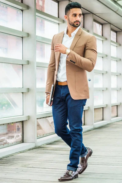Genç adam iş Casual kahverengi ceket, beyaz gömlek, mavi pantolon, siyah deri ayakkabı, kol saati, dizüstü bilgisayar, içinde kapalı geçit ayakta tutan giyen moda New York, sakallı,