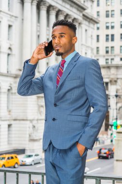 New York'ta, giyen karanlık gökyüzü mavi takım elbise, çalışma sakallı genç Afrikalı-Amerikalı işadamı mor kırmızı desenli kravat, vintage ofis binası, cep telefonuyla konuşurken dışarıda sokakta duran