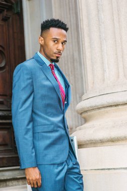 İşten sonra. New York'ta, giyen karanlık gökyüzü mavi takım elbise, çalışma sakallı genç Afrikalı-Amerikalı işadamı kravat, dizüstü bilgisayar, ofis binadan çıkıp tutan mor kırmızı desenli