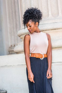 Genç Afro-Amerikan Kız afro saç modeli, beyaz kulak boncuk iğne ile kolsuz açık renk üst, koyu turuncu kemer, siyah etek, New York'ta ofis dışında ayakta aşağı bakıyor giyiyor