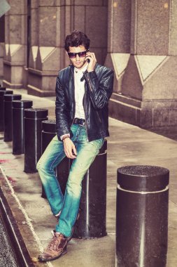 Siyah deri ceketli giyinme, mavi jeans, kahverengi önyükleme ayakkabıların güneş gözlüğü, New York, sokakta oturan sakallı bir genç Avrupa işadamı, cep telefonu üzerinde ara çalışma sırasında konuşurken.