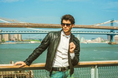 New York'ta seyahat Avrupa iş adamı. Giydiği siyah deri ceket, beyaz gömlek, güneş gözlüğü, harbor adlı duran sakallı genç adam düşünüyorum. Manhattan, Brooklyn köprüler arka plan üzerinde