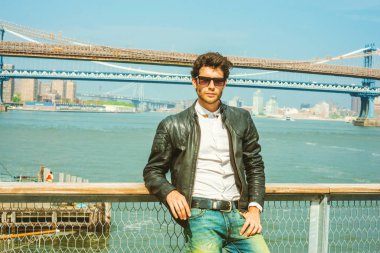New York'ta seyahat Avrupa iş adamı. Giydiği siyah deri ceket, beyaz gömlek, güneş gözlüğü, harbor adlı duran sakallı genç adam düşünüyorum. Manhattan, Brooklyn köprüler arka plan üzerinde