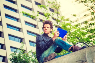 Okuma gücünü. Küçük, mavi tablet bilgisayar iş bölgesi duvarda üst kısmında okuma genç bir adam. Yeşil ağaçlar, güçlü güneş zemin üzerine Parlatıcı. Teknoloji günlük hayatta.