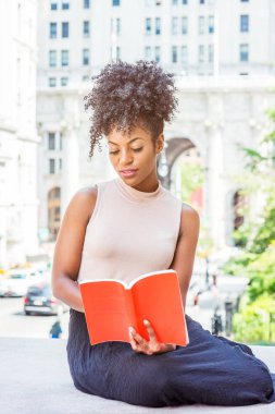 Okuma dışında. Kırmızı kitap okuma aşağı, bacaklar, New York, vintage tarzı ofis tarafından sokakta oturan bükme genç Afro-Amerikan Bayan üniversite öğrencisi afro saç modeli ile seyir.