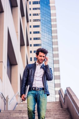 Dizüstü bilgisayar taşıma, ancak ailesine cep telefonunu, merdivenlerden inip çalıştıktan, eve gitmek sonra ofis binası dışında yürüyüş konuşurken genç profesyonel, kolu. Mor renk tonu ile filtre uygulanmış görünüm.