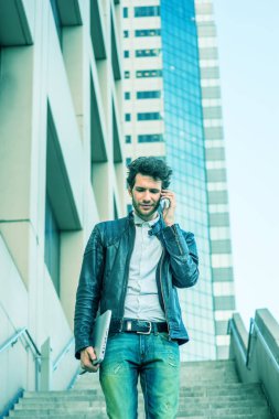 Dizüstü bilgisayar taşıma, ancak ailesine cep telefonunu, merdivenlerden inip çalıştıktan, eve gitmek sonra ofis binası dışında yürüyüş konuşurken genç profesyonel, kolu. Mavi renk tonu ile filtre uygulanmış görünüm.
