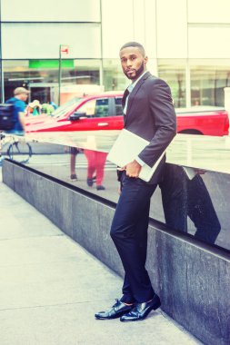 Genç Afrikalı-Amerikalı işadamı sakallı, afro kısa saç, siyah takım elbise, deri ayakkabı, dizüstü bilgisayar, Manhattan'ın Middletown, sokakta ayakta tutan giyen New York'ta seyahat arıyorum bana yardımcı olanvarmı