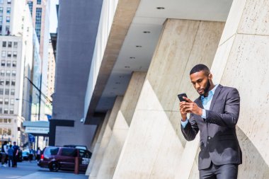 Okuma mesajları ayakta aşağı, seyir street, güneş altında sütun tarafından genç Afrikalı-Amerikalı işadamı sakal, kısa saçlı, New York City, giyen siyah takım elbise, dışında cep telefonuyla mesaj