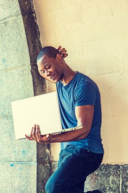 Genç Afro-Amerikan New York dışında dizüstü bilgisayarda çalışan adam, street, duvara karşı duran mavi V boyun T gömlek giymiş kol duvara, yetiştirme eller baş aşağı bakıyor, arka