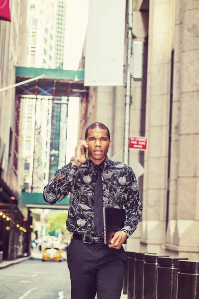 New York'ta zor Afrika kökenli Amerikalı iş adamı. Çiçek giyen desenli gömlek, kravat, taşıma dizüstü bilgisayar, sokakta yürürken, telefonda konuşurken genç adam. Zemin üzerine sarı taksi.