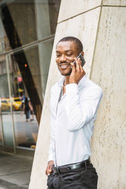 Telefon görüşmesi dışında. New York'ta ofis dışında sokakta duran beyaz gömlek giymiş genç Afrikalı-Amerikalı işadamı sakallı, aşağı bakıyor, gülümseyen, cep telefonuyla konuşmak
