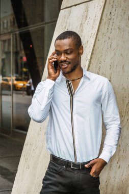 Telefon görüşmesi dışında. New York'ta ofis dışında sokakta duran beyaz gömlek giymiş genç Afrikalı-Amerikalı işadamı sakallı, aşağı bakıyor, gülümseyen, cep telefonuyla konuşmak