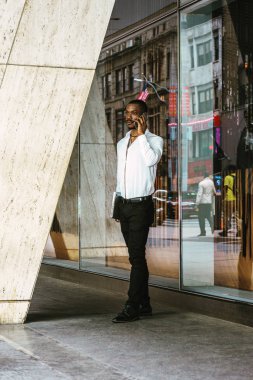 New York'ta, giyen beyaz gömlek, siyah pantolon, deri ayakkabı, çalışan genç Afrikalı-Amerikalı işadamı dizüstü bilgisayar, Ofis Binası, duran taşıyan cep telefonuyla konuşurken, düşünme