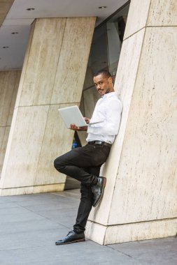 New York'ta, giyen beyaz gömlek, siyah pantolon, deri ayakkabı, bina, dizüstü bilgisayarda çalışarak, düşünme ofis dışında sütun karşı ayakta çalışma genç Afrikalı-Amerikalı işadamı