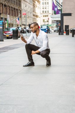 Sakallı, genç Afrikalı-Amerikalı beyaz gömlek, siyah pantolon, deri ayakkabı, cep telefonunuzda ileti okuma sokakta Manhattan, New York, çömelme giyen adam. Arabalar, adam binalarda
