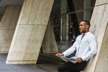 Bina, dizüstü bilgisayarda çalışarak, seyir, düşünme ofis dışında sütun karşı New York'ta, giyen beyaz gömlek, siyah pantolon, çalışan genç Afrikalı-Amerikalı işadamı duran