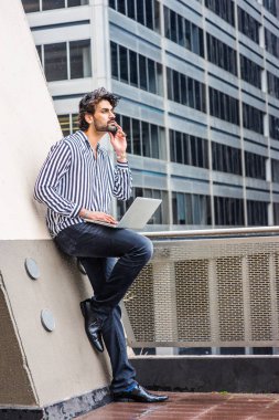 Yağmur - grenli, yağmurlu, ıslak hissediyorum. Çizgili gömlek giyen genç işadamı, siyah pantolon, deri ayakkabı, New York'ta ofis binasının önünde duran, dizüstü bilgisayarda çalışan, telefonda konuşan