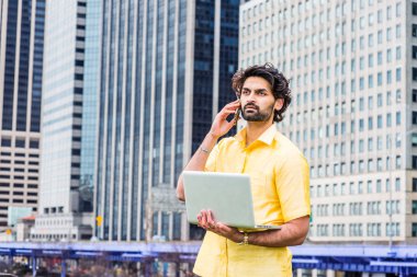 Yağmur gün- grenli, ıslak hissediyorum. Sakallı genç Doğu Hint Amerikalı Adam New York'ta seyahat, sarı takım elbise giyiyor, yüksek binaların önünde duran, dizüstü bilgisayar tutan, telefon konuşurken