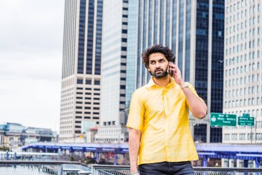 Yağmur günü - grenli, ıslak hissediyorum. Sakallı genç Doğu Hint Amerikalı Adam New York'ta seyahat, sarı kısa kollu takım elbise giyiyor, modern yüksek binanın önünde duran, hücre telefon konuşurken