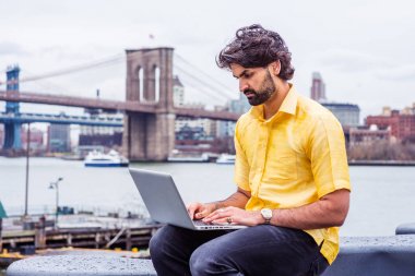 Yağmur - grenli, yağmurlu, ıslak hissediyorum. Sakallı genç adam New York'ta seyahat ediyor, kısa kollu sarı gömlek giyiyor, East River'da oturuyor, dizüstü bilgisayarda çalışıyor. Köprüler, arka planda tekne