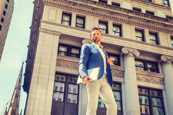 Genç Avrupa dört gözle işadamı seyahat, New York City bölgesindeki çalışma, mavi ceket, gri pantolon giyiyor, dizüstü bilgisayar holding, eski office bina dışında sokakta duran sakallı