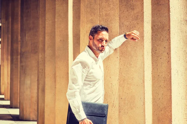 Dışarıda düşünüyorum. Sakallı, beyaz gömlekli, elinde evrak çantası tutan, New York'ta ofisin dışında duran, güneşin altında duran, kolkola sütuna yaslanmış, başka bir yere bakan, düşünen genç Avrupalı bir işadamı.