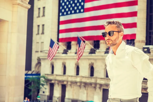 Yazın New York 'ta gezen sakallı genç bir Avrupalı. Uzun kollu beyaz gömlek, güneş gözlüğü takıyor. Eski tarz ofis binasının önünde duruyor.