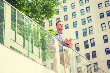 Başarıya Giden Yol. New York'ta okuyan genç yakışıklı Amerikalı öğrenci, yüksek binalar, yeşil ağaçlar, dizüstü bilgisayar üzerinde çalışan, yukarı bakıyor, düşünme ile iş bölgesinde cam korkuluk ayakta