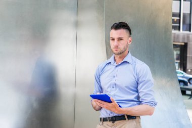 Modern Okuma. Açık mor, uzun kollu gömlek giyen, New York'ta sokakta gümüş metal duvar başında duran, mavi tablet bilgisayarı tutan eller, okuma, bakma, düşünme