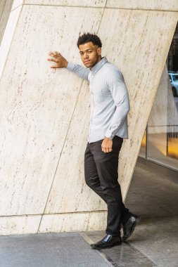 New York'ta Genç Yakışıklı Amerikan Adam Portresi, açık gri uzun kollu gömlek giyiyor, siyah pantolon, deri ayakkabı, sokakta ofis binası dışında duran, güvenle ileriye bakıyor