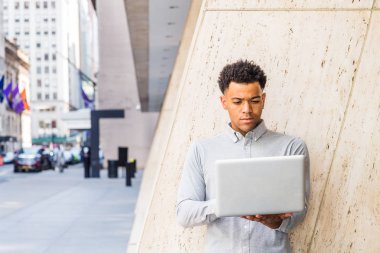 Başarıya Giden Yol. Genç Mix-Race American Man New York'ta çalışan, açık gri uzun kollu gömlek giyen, dizüstü bilgisayar tutan, ofis binası dışında sokakta duran, aşağı bakıyor, okuma