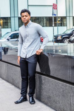 Genç Yakışıklı Amerikan Adam seyahat, New York'ta rahatlatıcı, açık gri uzun kollu gömlek giyiyor, siyah pantolon, deri ayakkabı, sokakta yarım mermer duvar tarafından ayakta, güvenle ileriye bakıyor