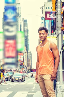 Genç Happy Mix Race American Man sıcak yaz aylarında New York'ta seyahat, turuncu tank top giyiyor, bej pantolon, Manhattan Times Meydanı'nda sokak kavşağında duran, seyir, gülümseyen