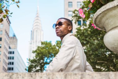 Genç Yakışıklı Afro-Amerikan Adam güneş gözlüğü takan, etrafa bakıyor, Manhattan dışında rahatlatıcı, New York. Yüksek binalar, arka planda ağaçlar