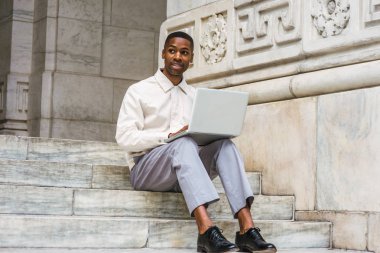 Başarıya Giden Yol. Afro-Amerikan Öğrenci açık renkli ceket giyiyor, gri pantolon, siyah deri ayakkabı, New York kampüsünde ofis binasının merdivenlerinde oturan, eğitim, dizüstü bilgisayar üzerinde çalışan