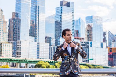 Genç Doğu Hint Amerikan Man siyah moda desenli alevler giyen, beyaz gömlek, New York'ta yüksek binalar ile iş bölgesinde ayakta, elleri siyah papyon tutan, ileriye bakıyor