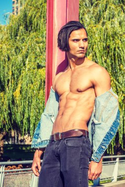 Genç Doğu Hint Amerikalı Adam mavi Denim ceket giyen, açıldı, yarı çıplak güçlü vücut gösteren, siyah kot pantolon, New York'ta parkta kırmızı direğe karşı duran, ciddi, uzağa bakıyor