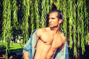 Genç Doğu Hint Amerikalı Adam mavi Denim ceket giyen, açıldı, yarı çıplak güçlü vücut gösteren, New York'ta söğüt ağacının uzun yaprakları altında duran, ciddi, uzağa bakarak, düşünme